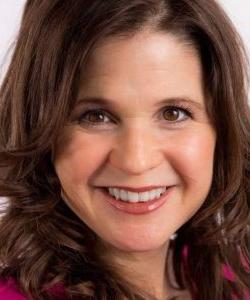 A close-up portrait of a smiling woman with brown hair wearing a Howard Payne University pink top. | HPU